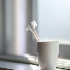 A simple, serene image of two toothbrushes in a white cup on a windowsill.